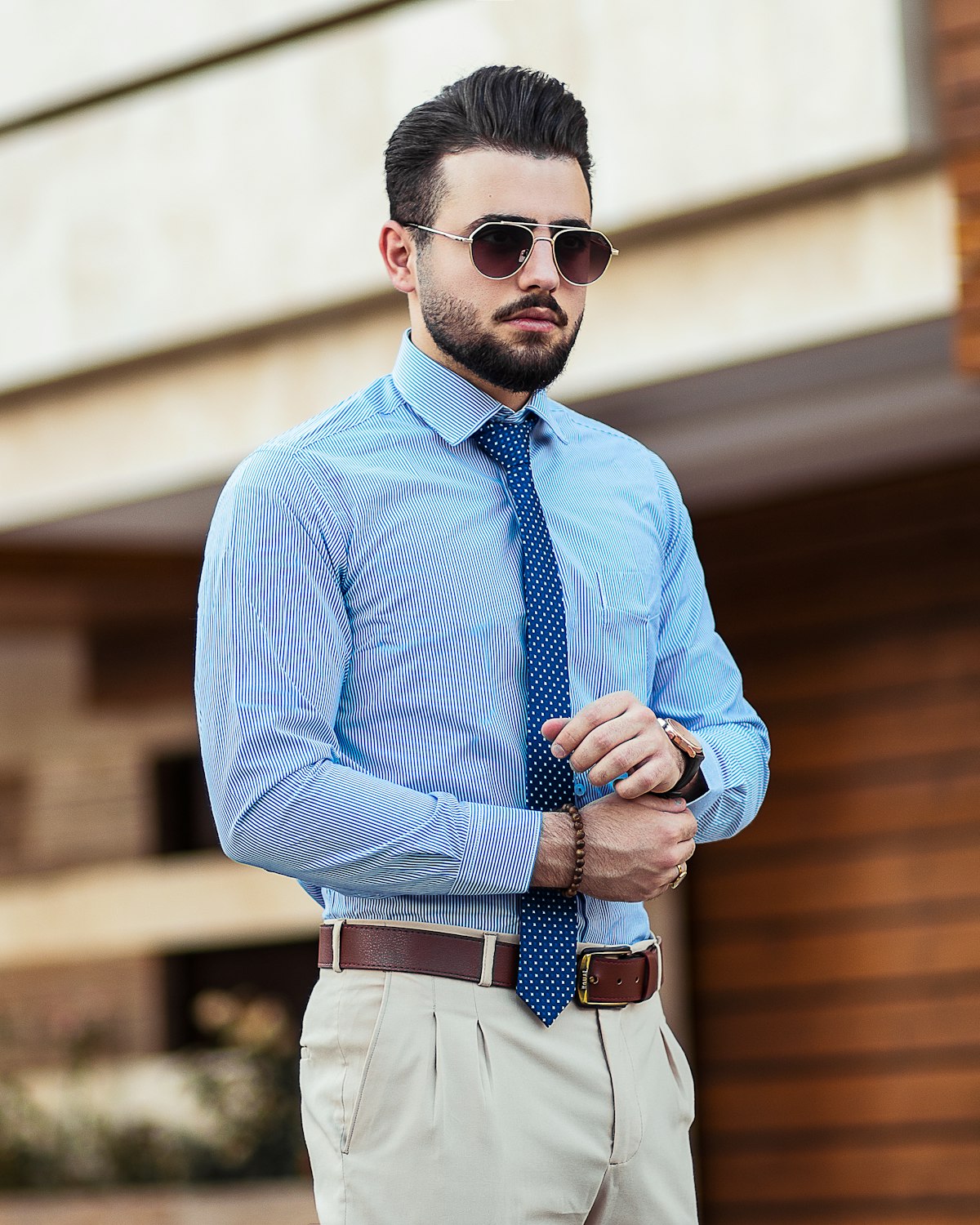 Man in a blue striped shirt and polka-dot tie adjusting his cuff