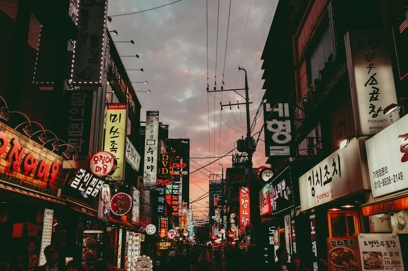 A Seoul shopping street at dusk under a pink sky