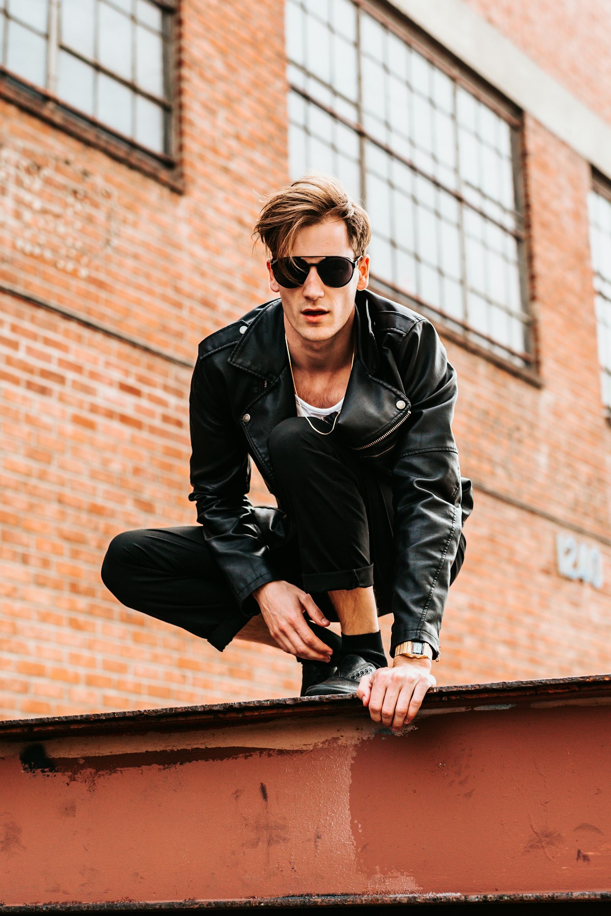 Young man in a black leather jacket and white tee against a SoHo-style brick warehouse wall